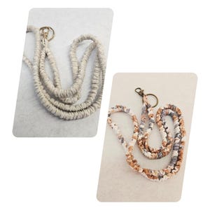 Op de afbeelding: Twee keycords met een macram&eacute; koordontwerp. E&eacute;n keycord is effen lichtbeige, terwijl de andere een meerkleurig koord is met tinten wit, bruin en grijs. Beide keycords zijn voorzien van een metalen ring en een karabijnhaak als bevestiging.