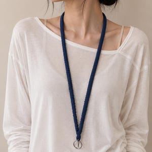 May include: A dark blue lanyard featuring a textured, braided cord design. The lanyard hangs in a V-shape around the neck and includes a circular silver-toned metal ring at the bottom for attaching items. The cord has a consistent, uniform appearance.