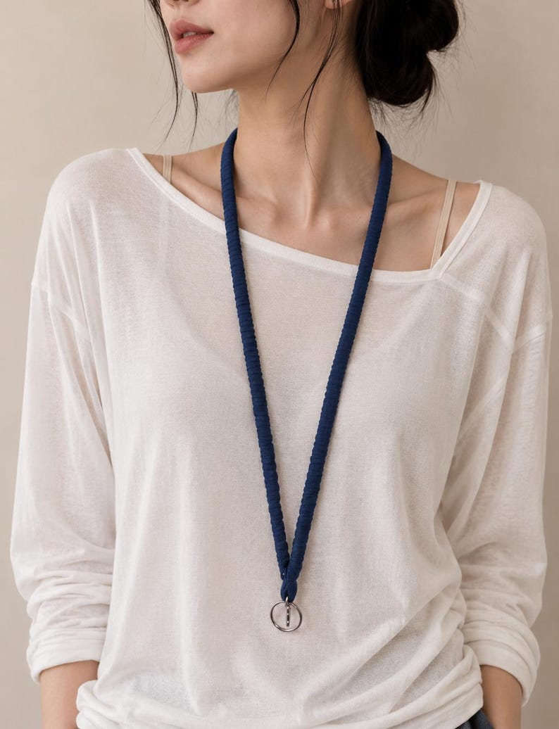 May include: A dark blue lanyard featuring a textured, braided cord design. The lanyard hangs in a V-shape around the neck and includes a circular silver-toned metal ring at the bottom for attaching items. The cord has a consistent, uniform appearance.