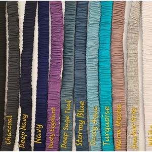 May include: A collection of eleven vertical fabric bands featuring a gathered, elasticized texture. The colors displayed from left to right are black, charcoal, deep navy, navy, dusty eggplant, deep sage teal, stormy blue, dusty aqua, turquoise, warm mocha, heather grey, and white.