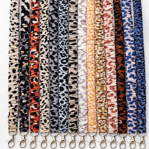 May include: A collection of lanyards in various animal print patterns, including leopard and cheetah designs. Each lanyard has a silver-colored clasp. The image includes a banner that reads "Many Colors Available."
