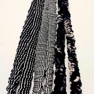 Puede incluir: Primer plano de varias tiras de tela con patrones en blanco y negro. Los patrones incluyen rayas y dise&ntilde;os texturizados. Las telas cuelgan sobre un fondo blanco, mostrando las diferentes texturas y patrones.