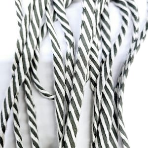 May include: A close-up of a bundle of white and dark green striped fabric cord. The cord is twisted and piled together.