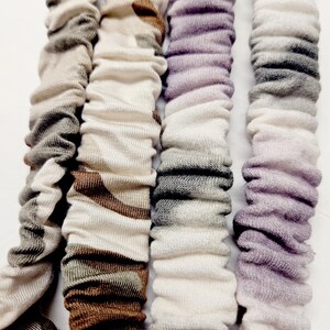 Puede incluir: Cuatro coleteros de tela en colores neutros. Los coleteros est&aacute;n alineados verticalmente y tienen un aspecto fruncido y texturizado. Los colores incluyen tonos de gris, marr&oacute;n y morado. Los coleteros est&aacute;n hechos de un material suave y el&aacute;stico.