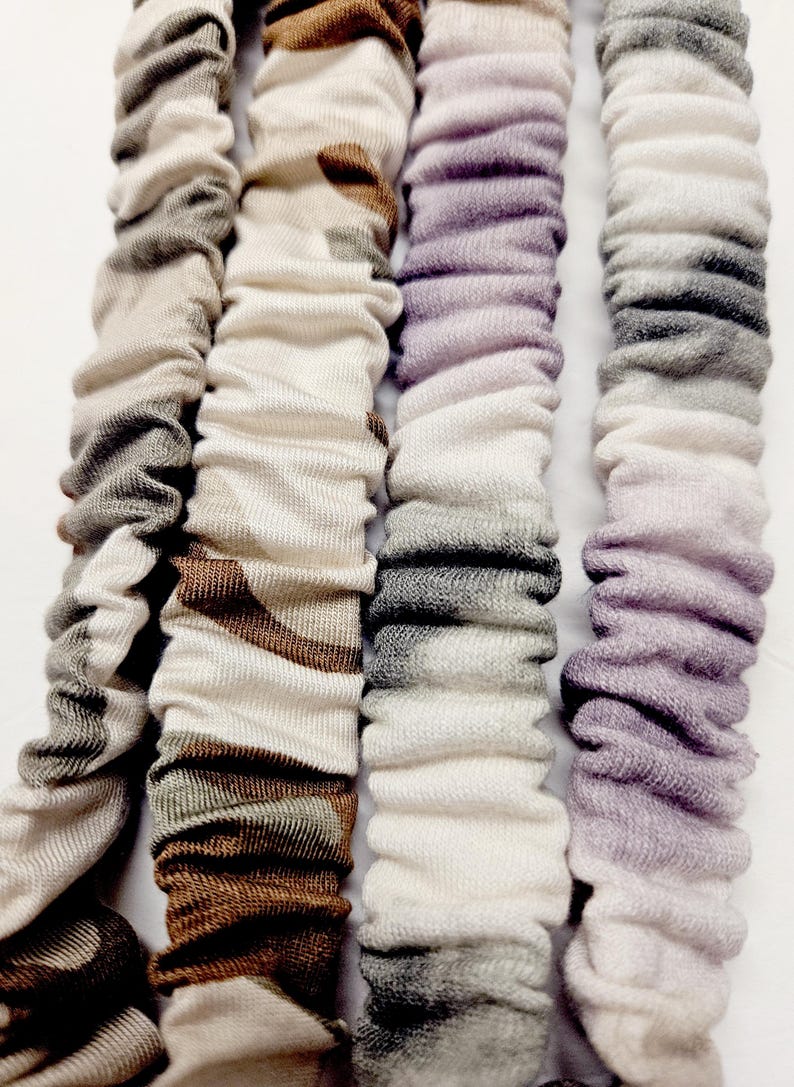 Puede incluir: Cuatro coleteros de tela en colores neutros. Los coleteros est&aacute;n alineados verticalmente y tienen un aspecto fruncido y texturizado. Los colores incluyen tonos de gris, marr&oacute;n y morado. Los coleteros est&aacute;n hechos de un material suave y el&aacute;stico.