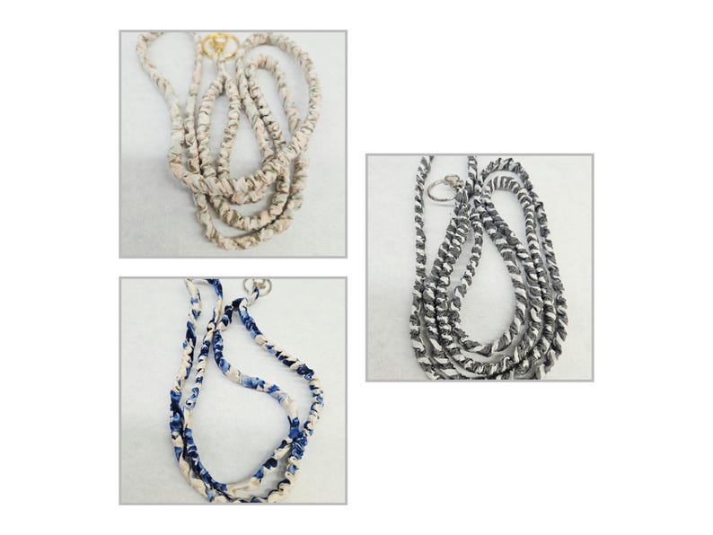 K&ouml;nnte beinhalten: Drei Stoff-Lanyards mit gedrehten Designs in Beige, Blau-Wei&szlig; und Schwarz-Wei&szlig;. Jedes Lanyard verf&uuml;gt &uuml;ber einen Metallring am oberen Ende und zeigt eine gewickelte Textilkonstruktion mit unterschiedlichen Farbmustern.