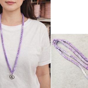 Op de afbeelding: Een lavendelkleurig stoffen koord met een geplooide, scrunchie-achtige textuur over de gehele lengte van de band. Het koord is voorzien van een zilverkleurige, draaibare karabijnhaak aan de onderkant voor het bevestigen van sleutels of badges.