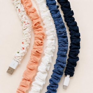 May include: A collection of USB charging cables with fabric sleeves in various colors. The cables include a floral print, peach, white, blue, and navy. Each cable has a USB connector on one end.