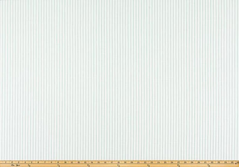 May include: White fabric with vertical, light blue stripes. The stripes are evenly spaced and run the length of the fabric. A wooden ruler is at the bottom of the image, providing scale.