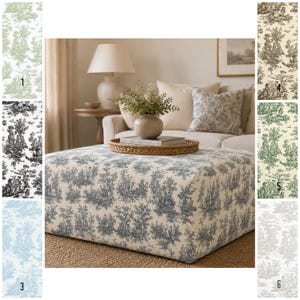 Op de afbeelding: Een grote, vierkante poef bekleed met blauw en wit toile de Jouy stof. De stof toont een gedetailleerde pastorale scène met bomen en figuren. De poef is het middelpunt van een woonkamer, met een bank en decor in neutrale tinten op de achtergrond.