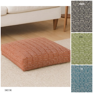 May include: A square floor cushion in a sandstone color with a repeating white wave pattern. The cushion is on a neutral-colored rug. The word "SANDSTONE" is printed at the bottom of the image. Additional color options are shown.