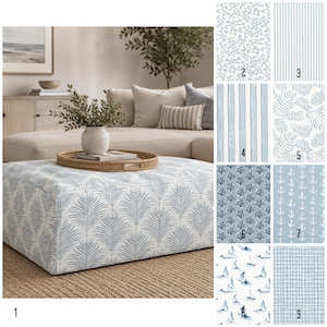 May include: A square ottoman with a light blue and white palm leaf pattern. The ottoman is in a living room setting with a neutral-toned sofa, a woven tray, and various fabric samples with different blue patterns.