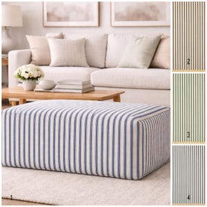 Puede incluir: Un otomán rectangular tapizado en tela a rayas azules y blancas. El otomán se coloca sobre una alfombra de color claro frente a un sofá blanco. Se muestran muestras de tela adicionales con rayas verticales en marrón, verde y negro.