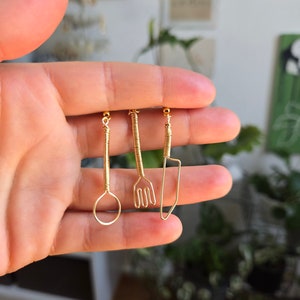 May include: Three gold wire earrings shaped like a spoon, fork, and knife.