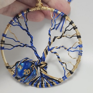May include: A gold wire tree of life pendant with blue and black wire branches. A blue 20-sided die is at the base of the tree. The pendant hangs from a 4-inch blue cord. The diameter of the pendant is 3.25 inches.