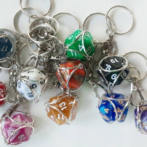 May include: A collection of ten colorful, wire-wrapped,  polyhedral dice keychains. The dice are in various colors, including red, green, blue, purple, and white. Each die has black numbers on its faces.