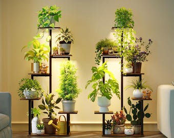 Puede incluir: Dos estanterías de metal marrón oscuro para plantas con múltiples estantes, cada una con varias plantas en macetas. Las plantas incluyen follaje verde frondoso, plantas con flores y cactus. Las estanterías están iluminadas con una luz cálida.