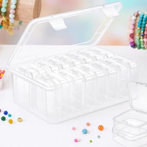 May include: A clear plastic storage box with multiple compartments, ideal for organizing small items. The lid is open, revealing the interior. Colorful beads and bracelets are visible in the background, suggesting the box's use for jewelry making supplies.