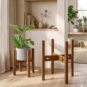 May include: Two adjustable bamboo plant stands with a natural wood finish. One stand holds a light gray cylindrical ceramic pot containing a green monstera plant with large, split leaves. The stands feature a cross-shaped base design.