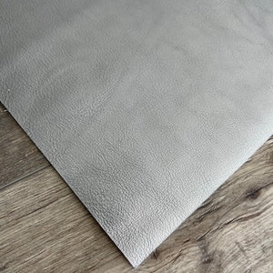 May include: A sheet of gray faux leather with a textured surface. The material is folded over, revealing the underside. The sheet is placed on a wooden surface.