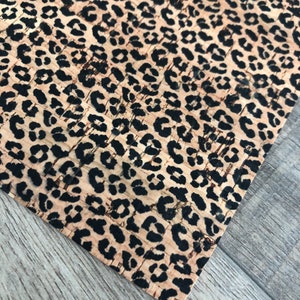 K&ouml;nnte beinhalten: Nahaufnahme einer Korkplatte mit Leopardenmuster. Das Muster zeigt schwarze Flecken auf beigem Hintergrund. Die Ecke der Platte ist sichtbar und zeigt die Textur des Materials und die Holzmaserung der Oberfl&auml;che.