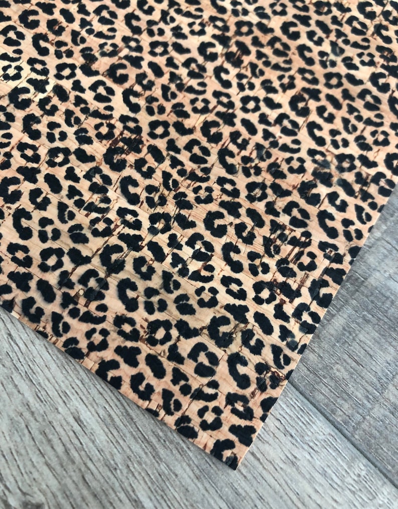 K&ouml;nnte beinhalten: Nahaufnahme einer Korkplatte mit Leopardenmuster. Das Muster zeigt schwarze Flecken auf beigem Hintergrund. Die Ecke der Platte ist sichtbar und zeigt die Textur des Materials und die Holzmaserung der Oberfl&auml;che.