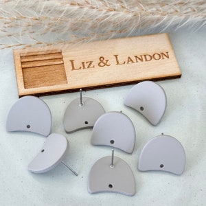 May include: Six pairs of gray half-circle earrings with silver posts. The earrings are displayed on a wooden surface with the text "Liz & Landon" engraved on it.