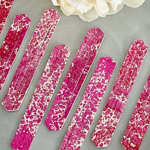 May include: A set of six pink and white marbled decorative sticks. The sticks are arranged in a staggered pattern, with the ends of the sticks pointing towards the top of the image.