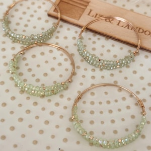 May include: Four gold wire bracelets with light green beads. The bracelets are arranged in a semi-circle on a white background with small gold dots.