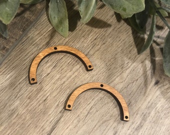 May include: Two unfinished wooden arches with three holes each. The arches are on a woodgrain surface.