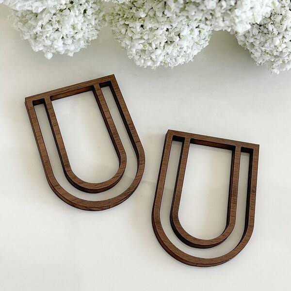 Op de afbeelding: Twee houten wanddecoraties in de vorm van een dubbel gelaagde U. De stukken zijn donkerbruin van kleur en hebben een gladde, gepolijste afwerking.