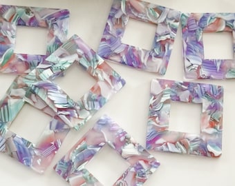 May include: Six square-shaped, colorful, translucent plastic embellishments with a square hole in the center. The embellishments have a marbled pattern in shades of pink, purple, green, and white.