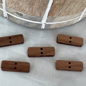 May include: Five brown wooden buttons with two holes each. The buttons are rectangular and have a natural wood grain.
