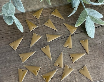 May include: A collection of twenty-one small, smooth, mustard-yellow triangular charms. Each charm features a single, centered hole near the top point, designed for attachment. The pieces have a glossy, uniform finish and are scattered across the surface.