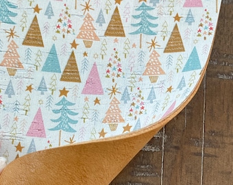 Puede incluir: Una hoja de tela de corcho blanco con un patrón repetitivo de árboles de Navidad rosas, azules y dorados y estrellas. La tela está doblada para revelar el respaldo de corcho marrón.