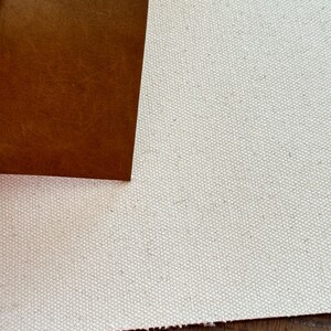 May include: Close-up of two fabric samples. One is a light beige canvas, and the other is a brown leather. The leather is smooth and has a slight sheen. The canvas has a textured appearance. The two materials are juxtaposed, showcasing their contrasting textures and colors.