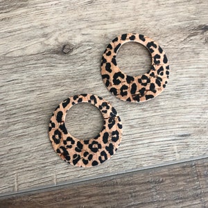 K&ouml;nnte beinhalten: Zwei runde Ohrringe mit Leopardenmuster. Die Ohrringe bestehen aus einem hellbraunen Material mit schwarzen Flecken. Die Ohrringe haben eine kreisf&ouml;rmige Form mit offenem Zentrum.