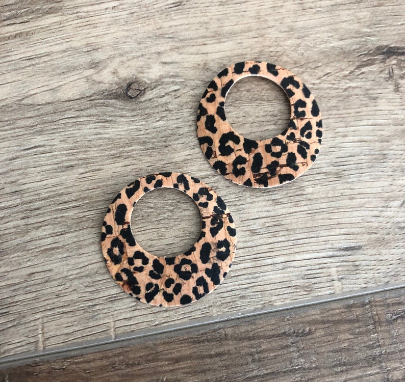 K&ouml;nnte beinhalten: Zwei runde Ohrringe mit Leopardenmuster. Die Ohrringe bestehen aus einem hellbraunen Material mit schwarzen Flecken. Die Ohrringe haben eine kreisf&ouml;rmige Form mit offenem Zentrum.