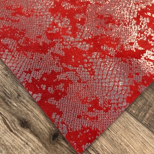 May include: Red fabric with a silver snakeskin pattern. The fabric has a glittery finish.