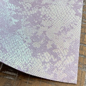 May include: A close-up of a piece of iridescent purple faux snakeskin fabric with a white snakeskin pattern.