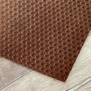 May include: A close-up of a brown leather sheet with a repeating embossed pattern of small stars.