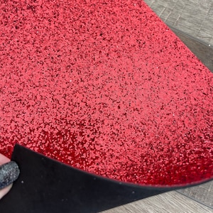 May include: Red glitter fabric with a black backing. The fabric is textured with small glitter particles.