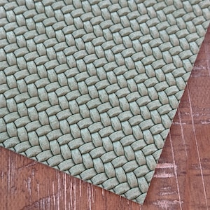 May include: A close-up of a green woven fabric with a textured surface. The fabric has a subtle sheen and a slightly raised pattern.