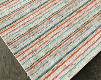 May include: A sheet of cork with a striped pattern in shades of orange, blue, and white. The cork has a natural, rustic look.