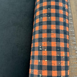 May include: A roll of black and orange cork fabric with a buffalo plaid pattern. The fabric has a textured surface.