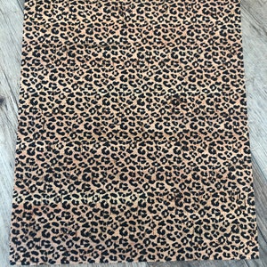 K&ouml;nnte beinhalten: Ein rechteckiges Blatt Kork mit einem Leopardenmuster. Das Muster hat schwarze Flecken auf einem beigefarbenen Hintergrund. Das Korkblatt liegt auf einer grauen Holzoberfl&auml;che.