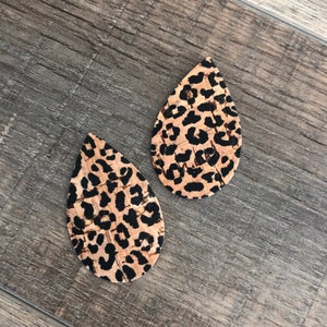 K&ouml;nnte beinhalten: Zwei tropfenf&ouml;rmige Ohrringe mit Leopardenmuster. Die Ohrringe haben einen beigefarbenen Hintergrund mit schwarzen Flecken. Die Ohrringe sind aus Kork gefertigt.