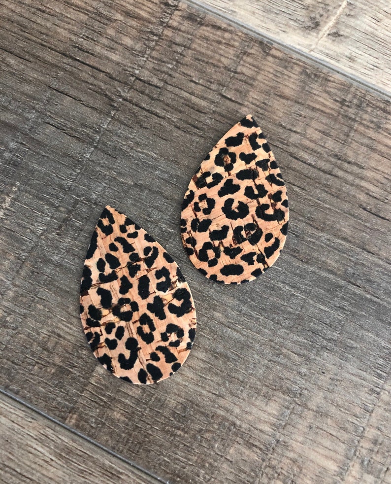 K&ouml;nnte beinhalten: Zwei tropfenf&ouml;rmige Ohrringe mit Leopardenmuster. Die Ohrringe haben einen beigefarbenen Hintergrund mit schwarzen Flecken. Die Ohrringe sind aus Kork gefertigt.