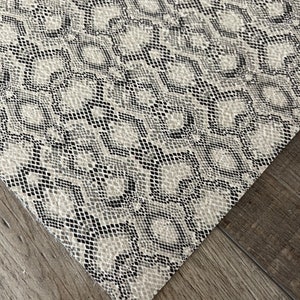 May include: Close-up of a white and black snakeskin patterned fabric. The fabric has a textured surface and a subtle sheen.