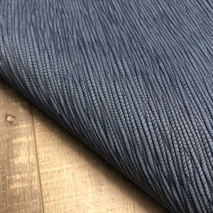 May include: A close-up of a dark blue textured fabric with a subtle woven pattern. The fabric is folded over a light brown wooden surface.